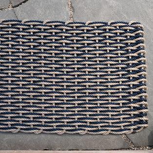 Handwoven sand and navy braided rope doormat with a tight weave pattern on a stone surface.