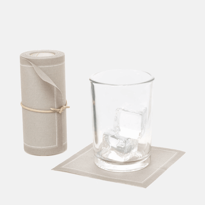Roll of 50 sand tear-off cotton cocktail napkins, with one napkin under a glass with ice.