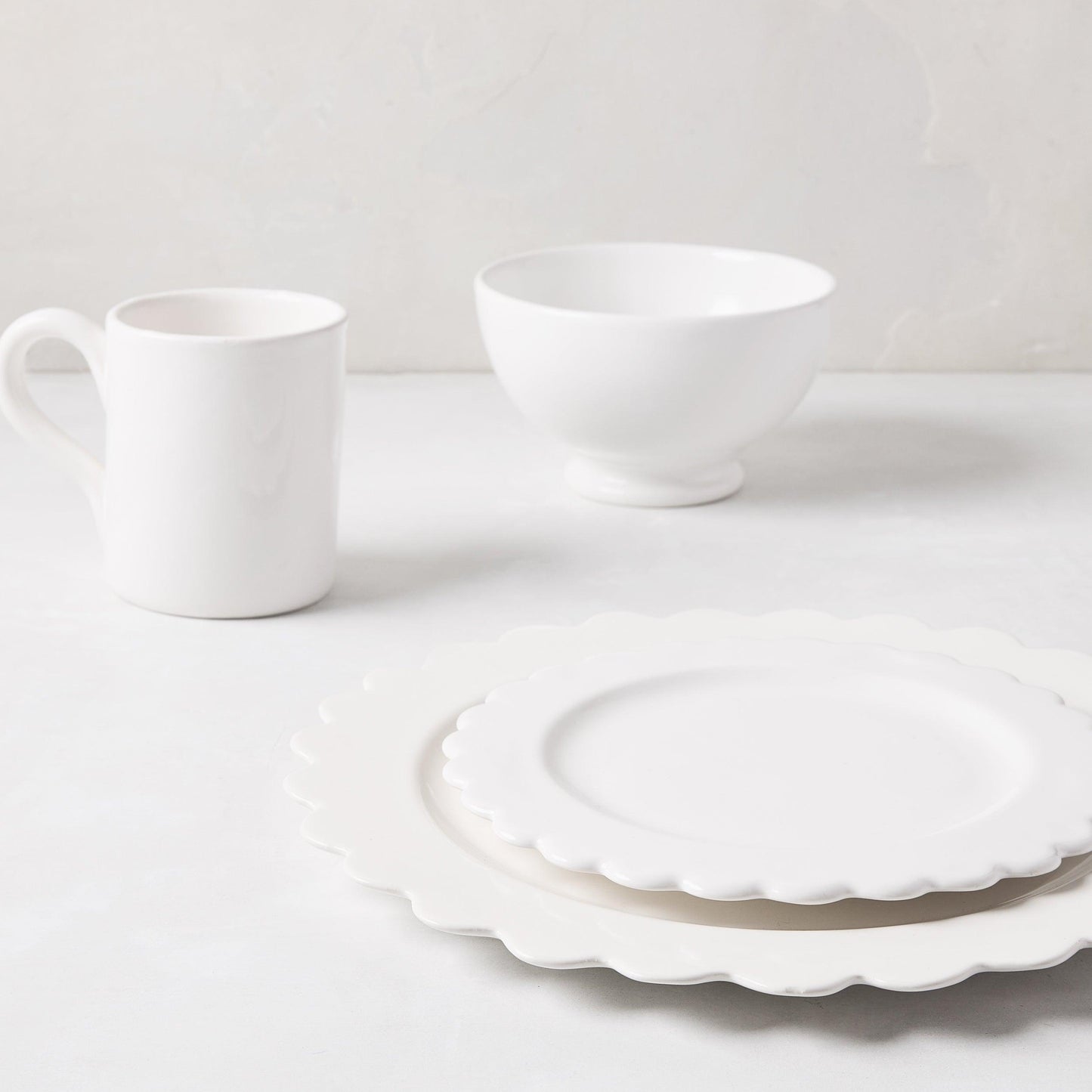 White ceramic scalloped dinner plate layered with a matching salad plate, mug, and bowl.