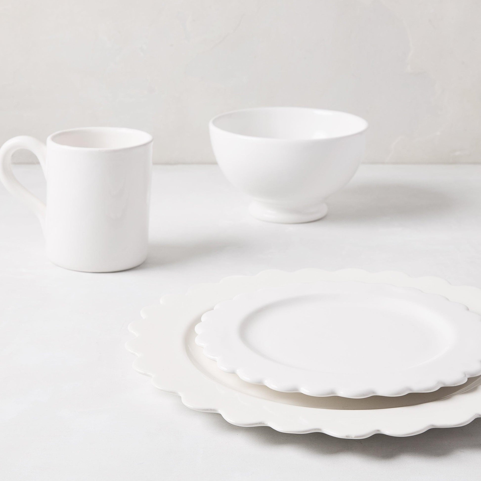 White ceramic scalloped dinner plate layered with a matching salad plate, mug, and bowl.