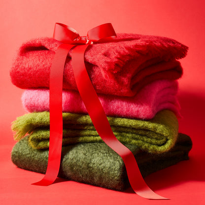 Stack of four folded mohair throws: red, magenta pink, lime green, and dark green, tied with a red ribbon.