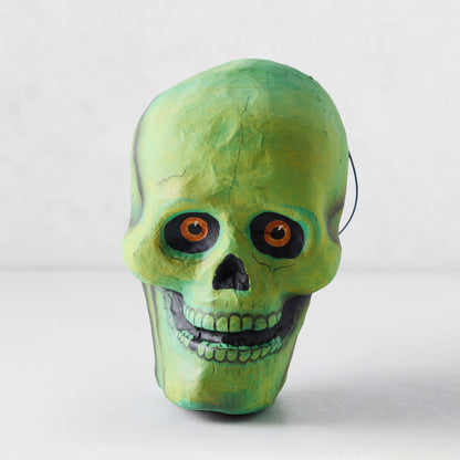 Handcrafted green papier-mâché skull candy bucket with distressed finish and orange eyes for Halloween decor.