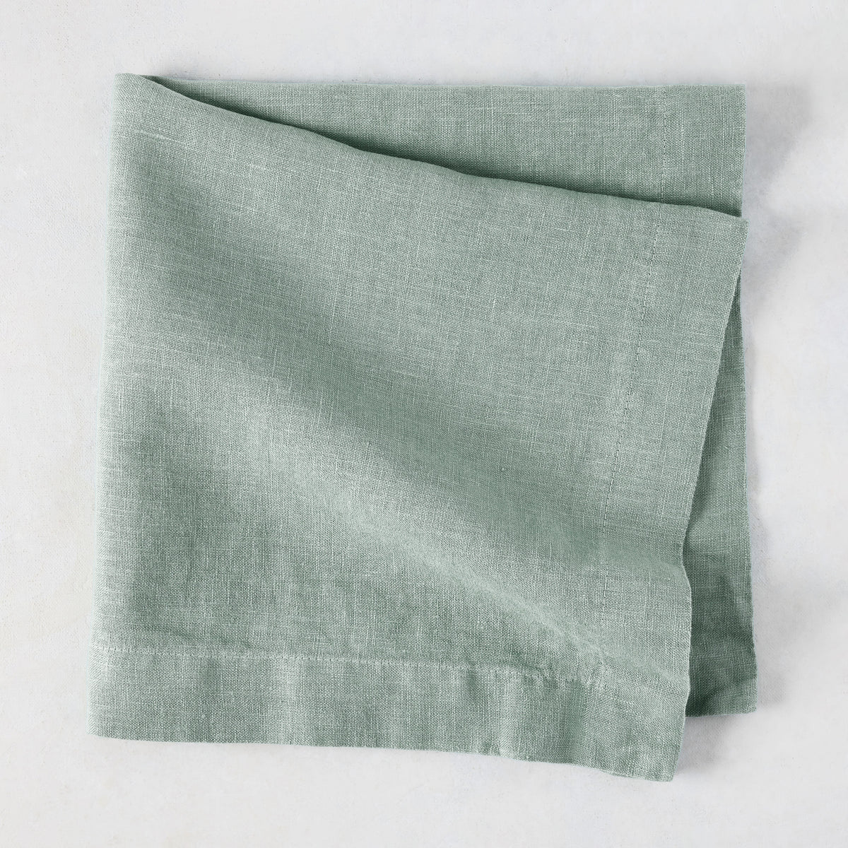 Sea Glass HG Signature hand-dyed linen napkin, folded, showing soft blue-aqua color and natural texture.