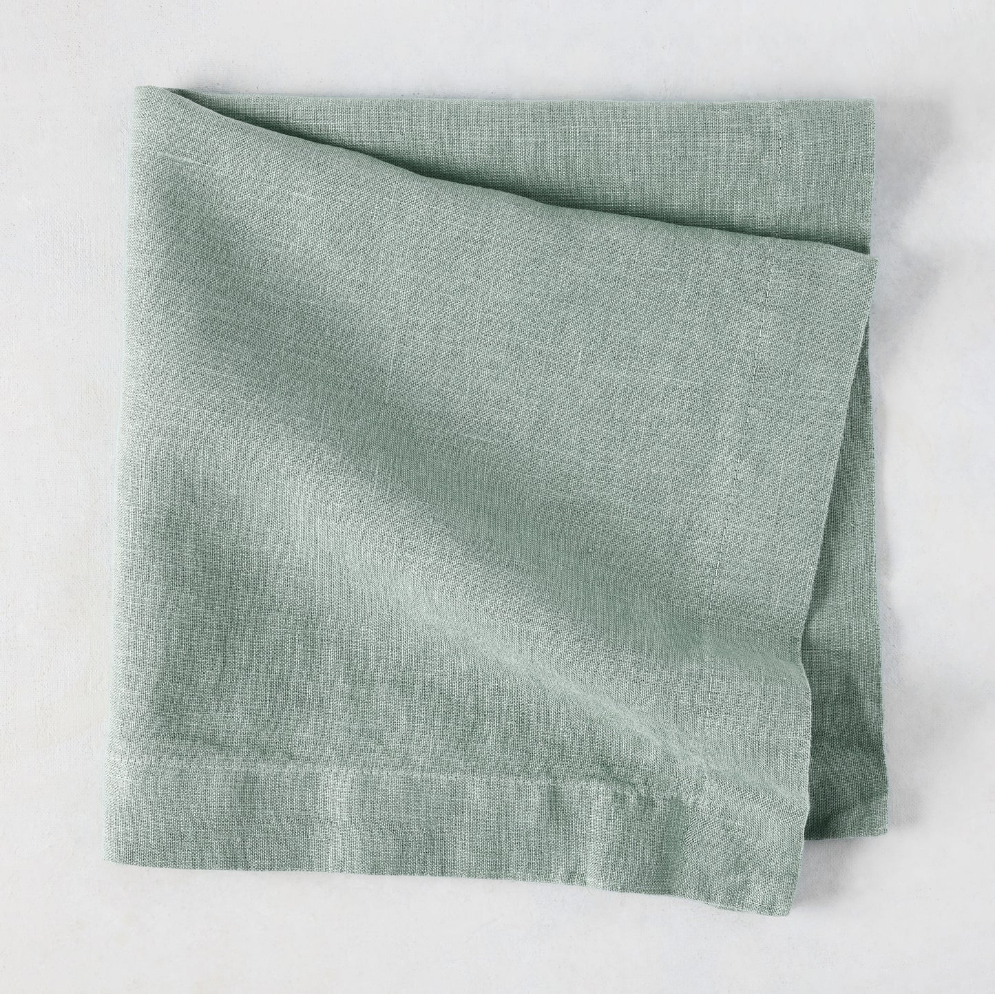 Sea Glass HG Signature hand-dyed linen napkin, folded, showing soft blue-aqua color and natural texture.