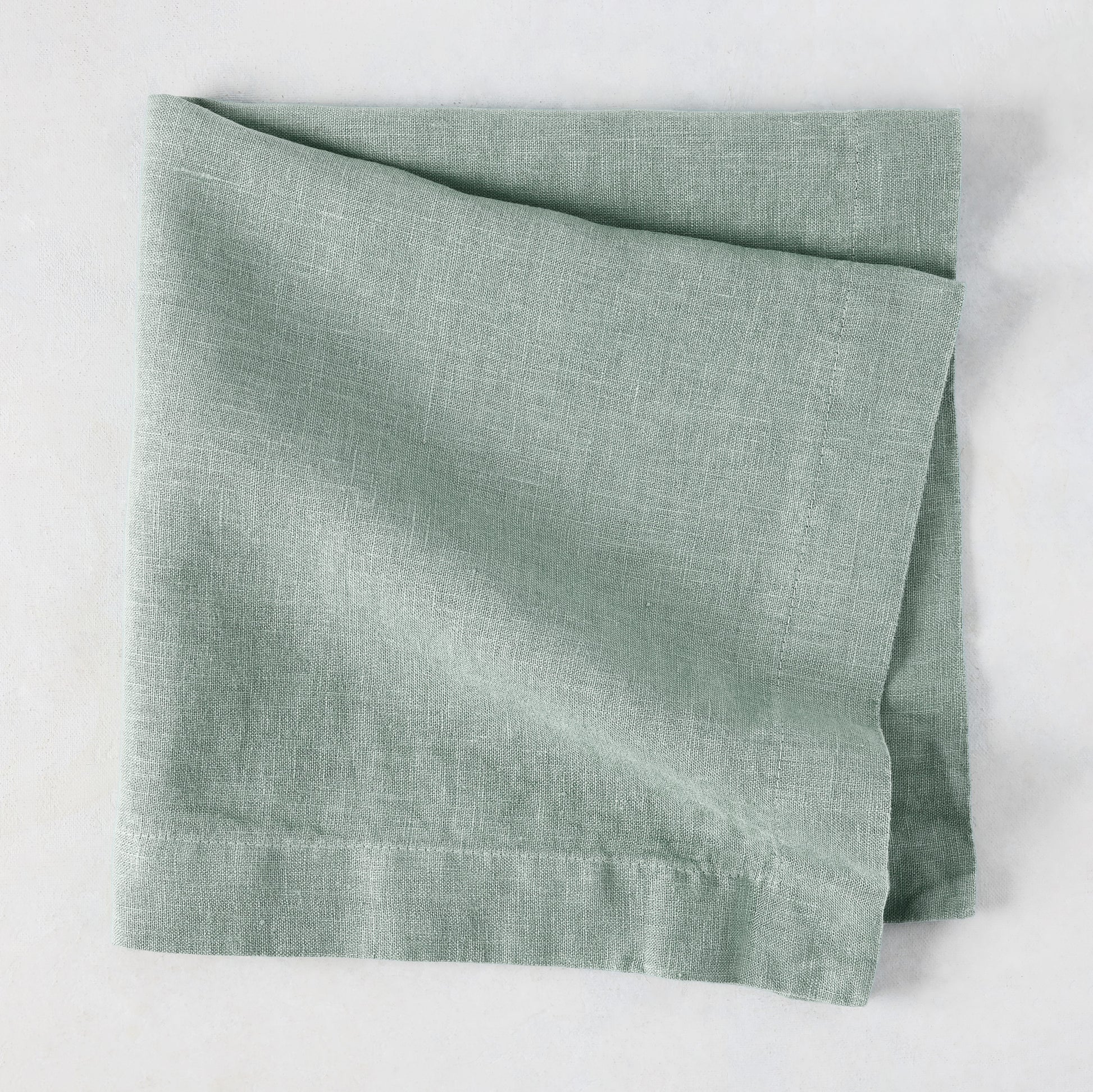Sea Glass HG Signature hand-dyed linen napkin, folded, showing soft blue-aqua color and natural texture.