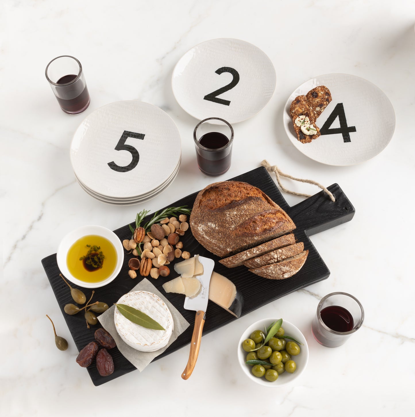Cream ceramic salad plates with black numbers 2, 4, 5, arranged with a charcuterie board and wine.