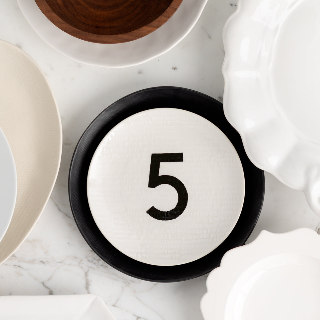 Cream ceramic salad plate with black number 5, hammered finish, on a black dinner plate.