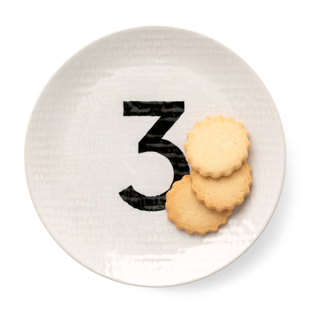 Cream ceramic salad plate with black number 3, hammered finish, holding three scalloped cookies.