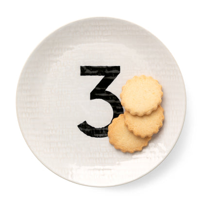 Cream ceramic salad plate with black number 3, hammered finish, holding three scalloped cookies.