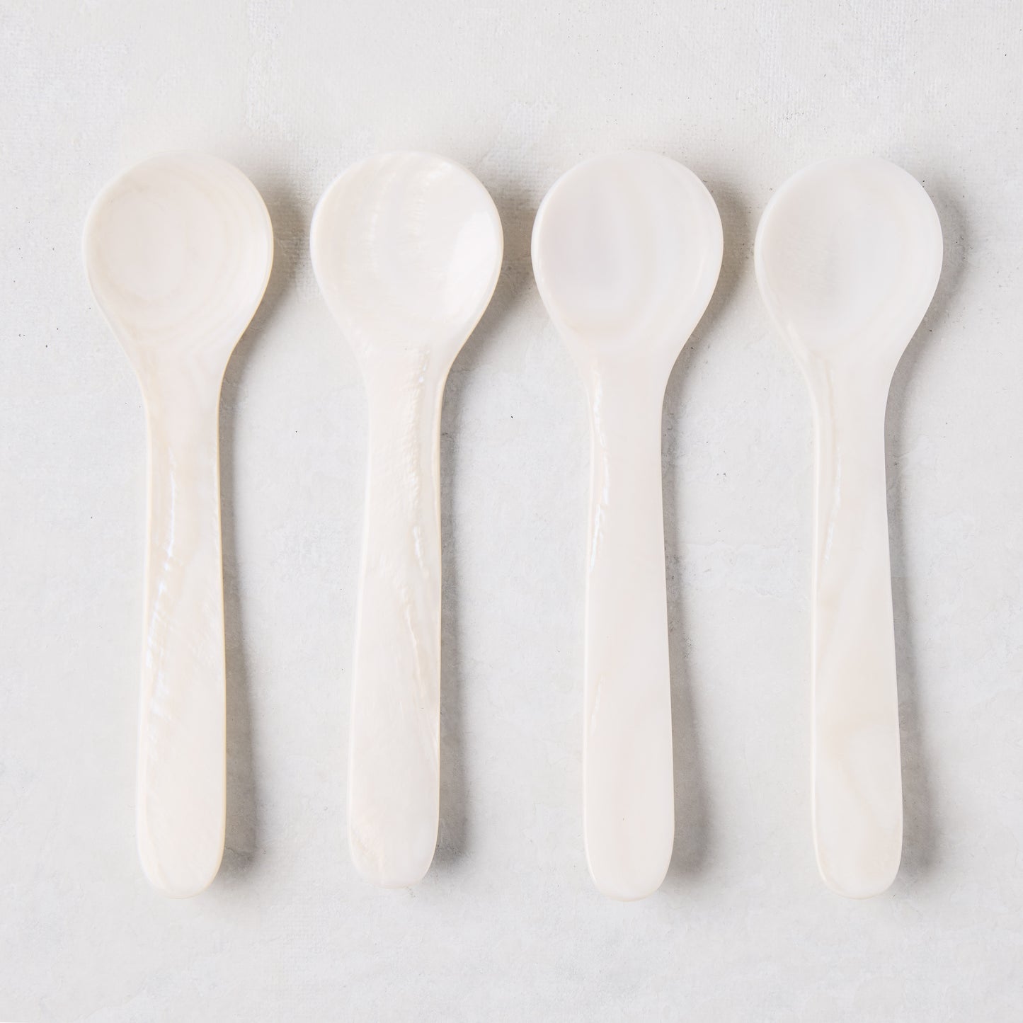 Four iridescent Mother of Pearl shell caviar spoons, 3.25"L, in a row on a light background.