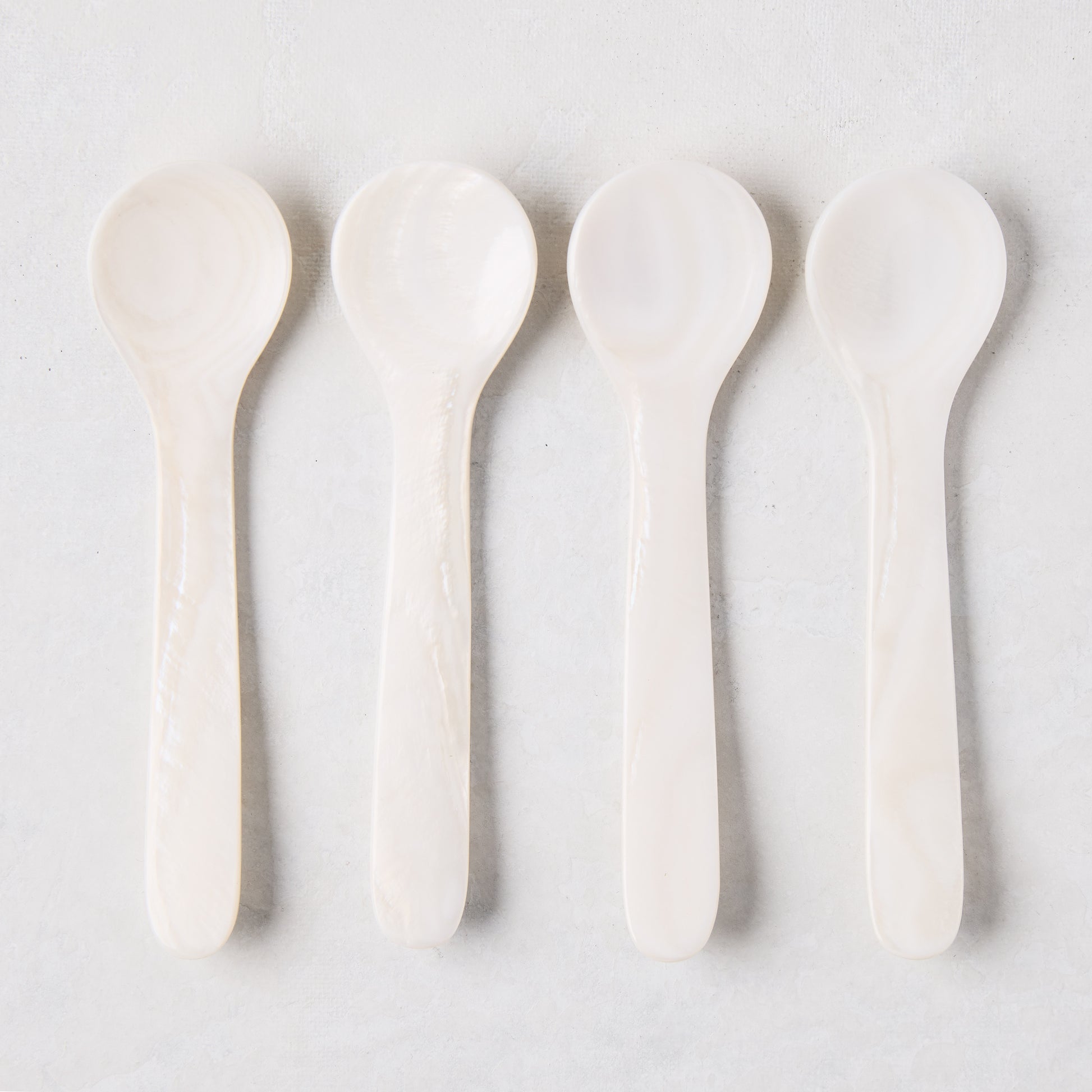 Four iridescent Mother of Pearl shell caviar spoons, 3.25"L, in a row on a light background.