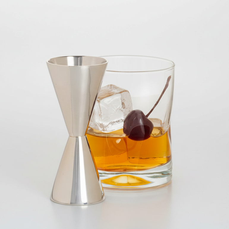 HG Silverplate Double Jigger with a gleaming finish, next to a whiskey glass with ice and a cherry.