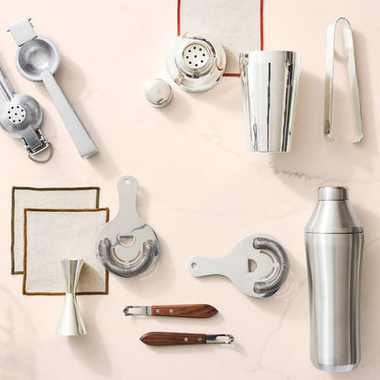 Silver HG Silverplate Ice Tongs, a key bar tool, shown with other cocktail accessories on a light marble surface.