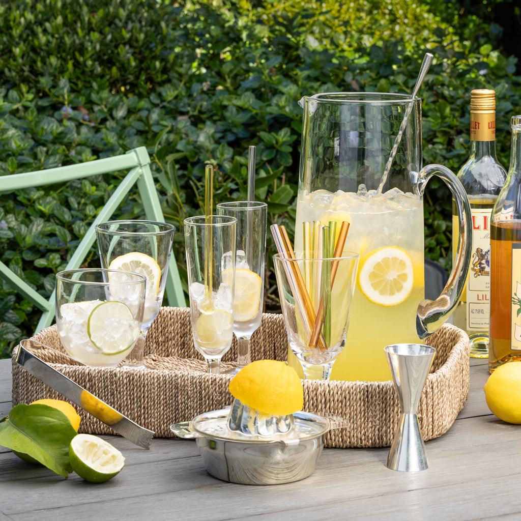 Silverplate ice tongs with a textured handle, resting on a woven tray with lemonade and bar tools.