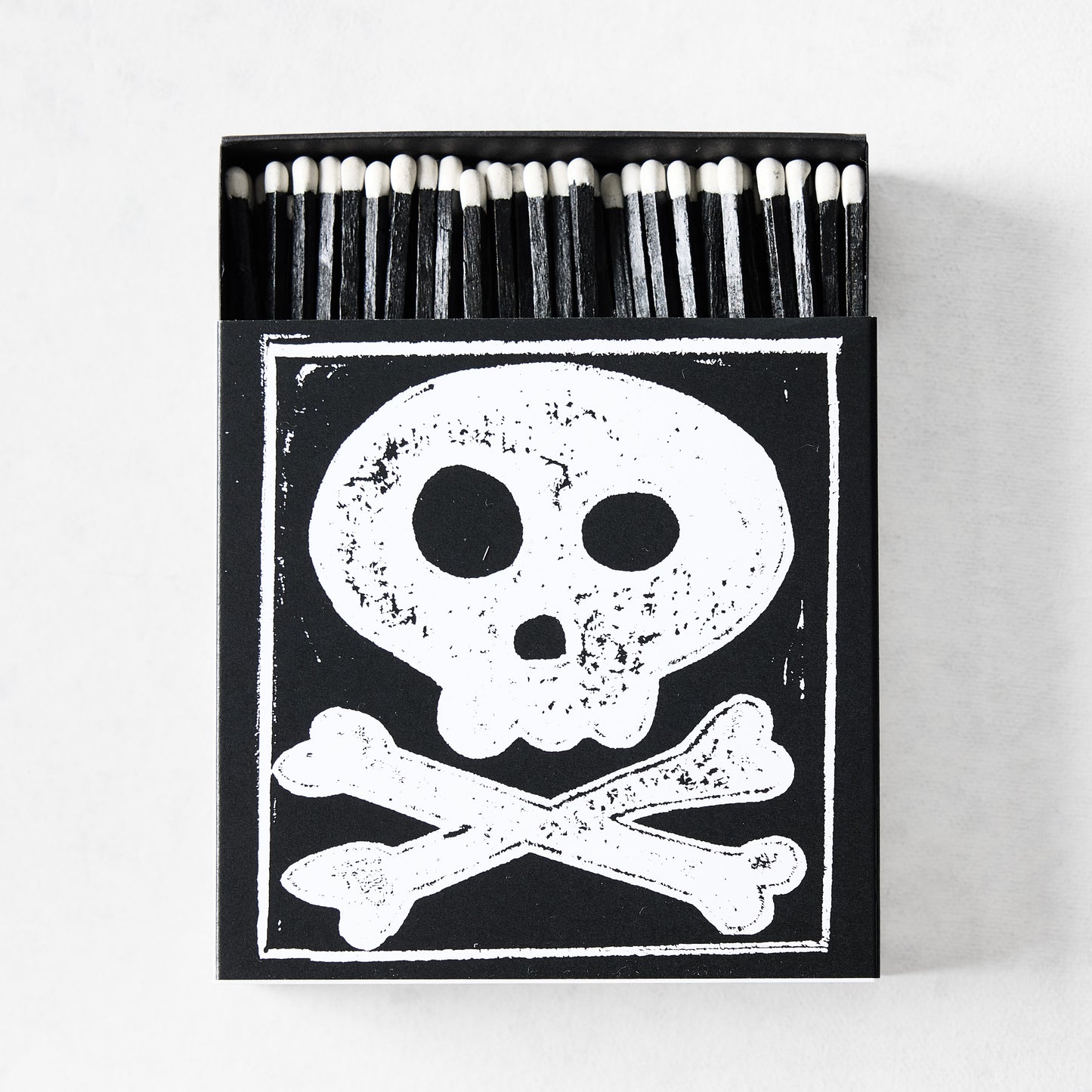 Black box of oversized matches featuring a white skull and crossbones print with black-tipped 4-inch matchsticks.