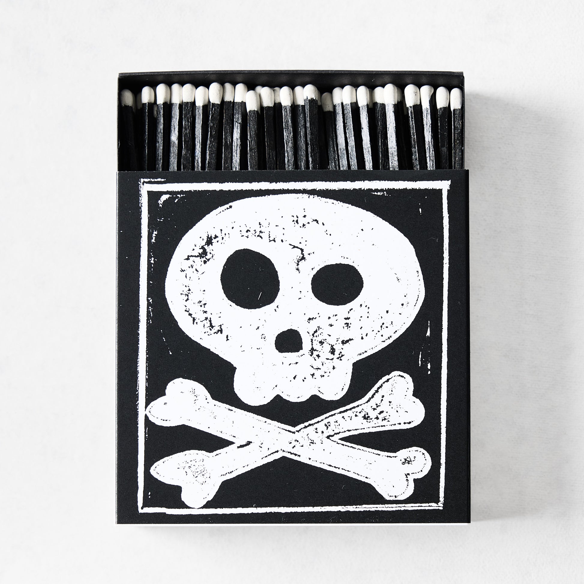 Black box of oversized matches featuring a white skull and crossbones print with black-tipped 4-inch matchsticks.
