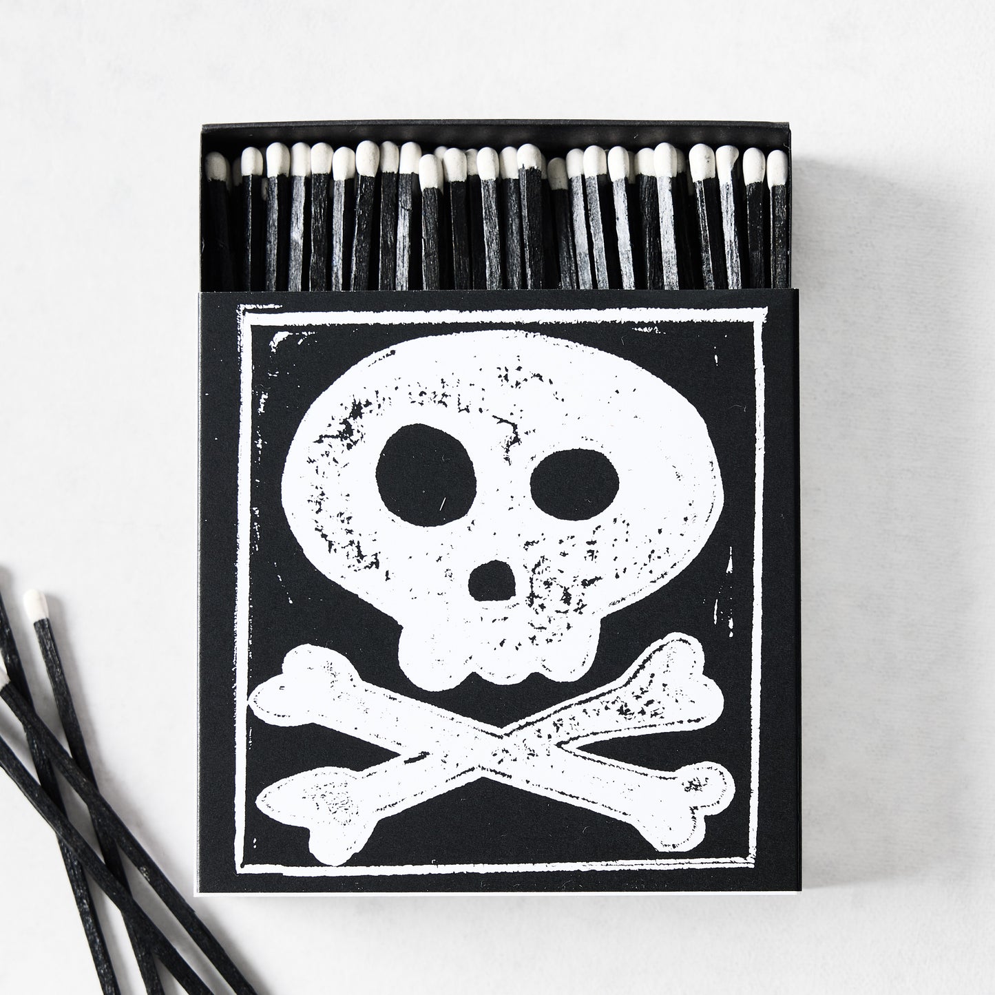 Black box of oversized matches featuring a white skull and crossbones design with black matchsticks and white tips.