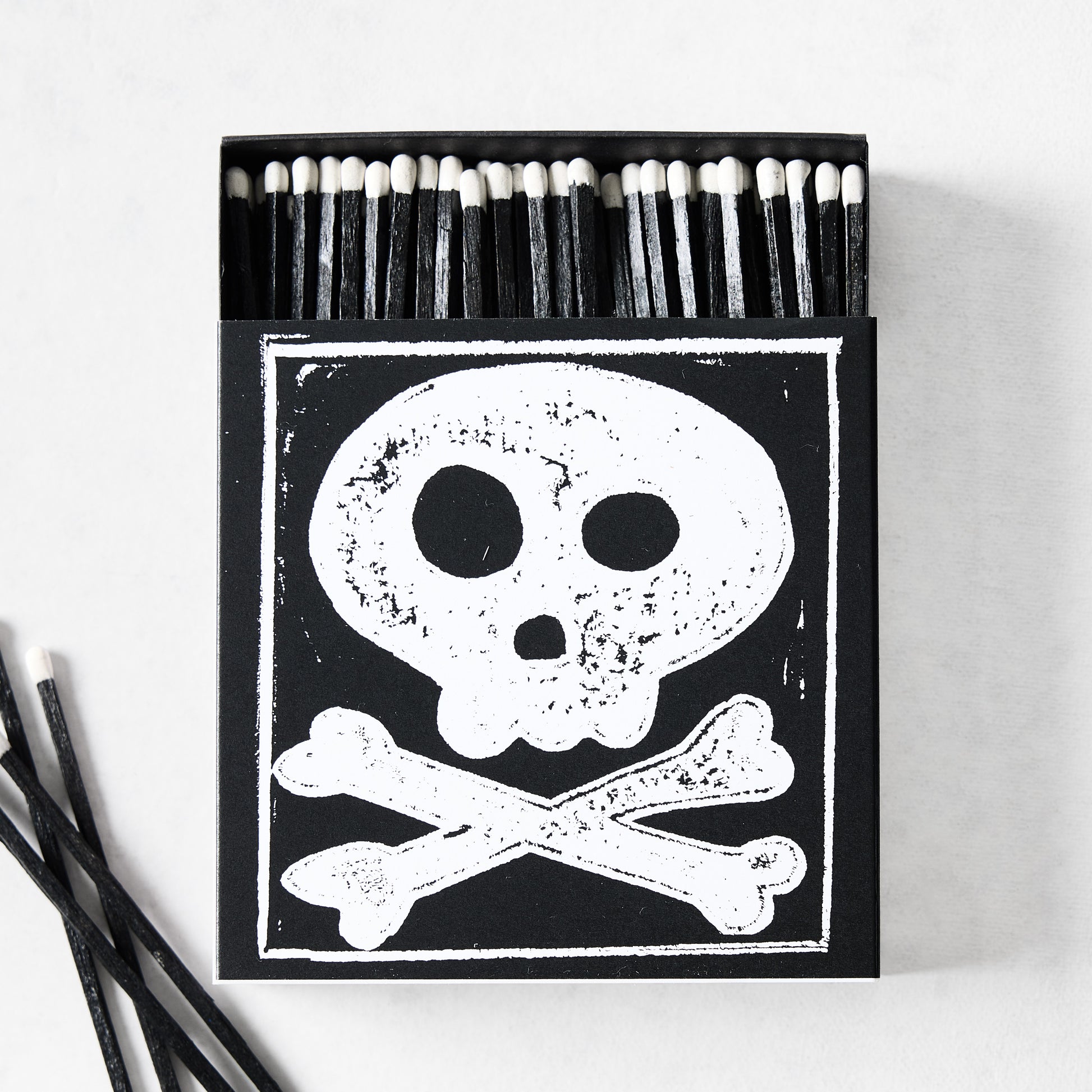 Black box of oversized matches featuring a white skull and crossbones design with black matchsticks and white tips.