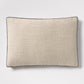 Linen lumbar pillow with a textured beige fabric and dark grey piping, 20"L x 14"H.