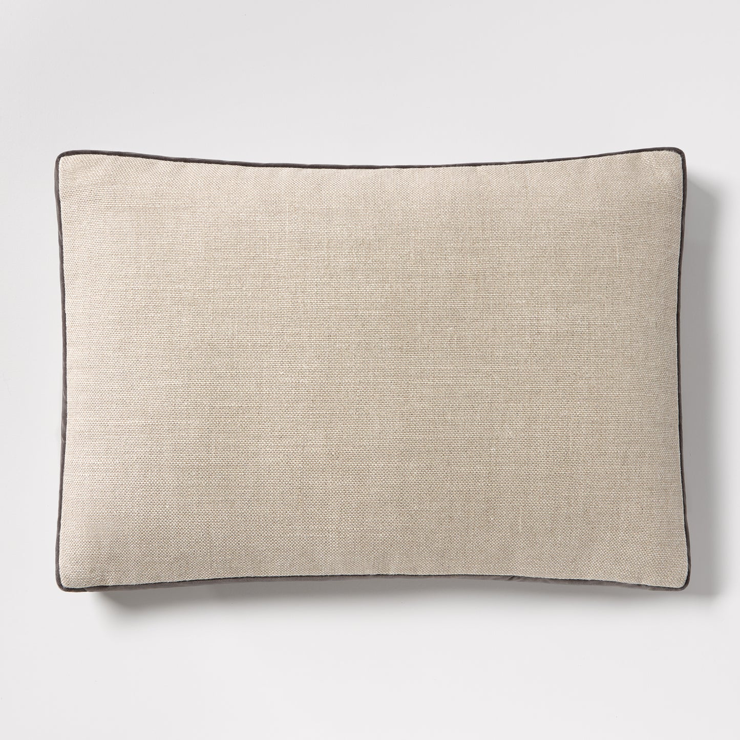 Linen lumbar pillow with a textured beige fabric and dark grey piping, 20"L x 14"H.
