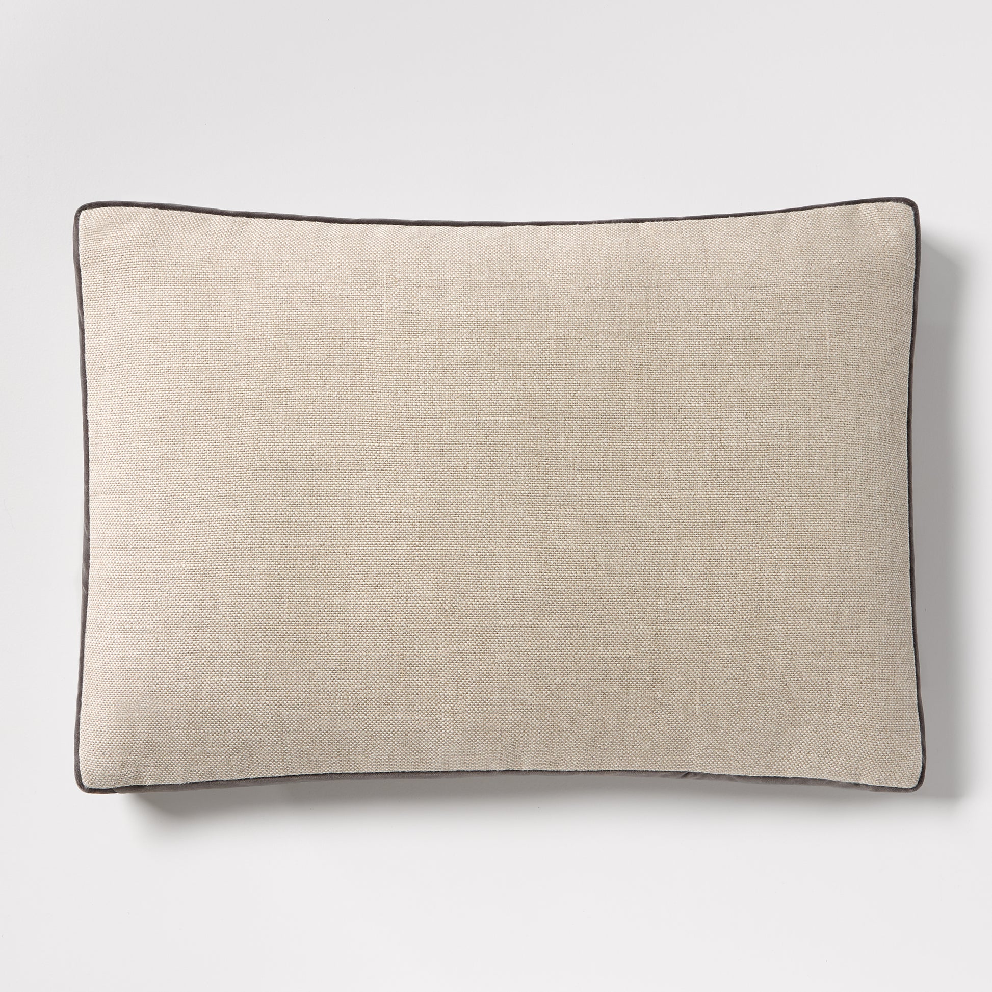 Linen lumbar pillow with a textured beige fabric and dark grey piping, 20"L x 14"H.