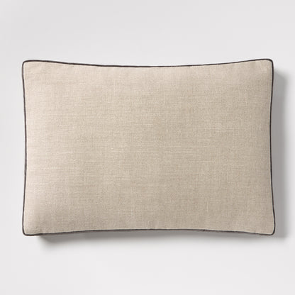 Linen lumbar pillow with a textured beige fabric and dark grey piping, 20"L x 14"H.