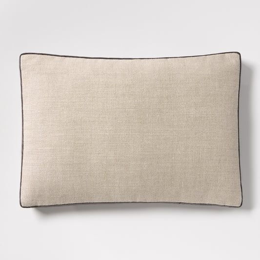 Linen lumbar pillow with a textured beige fabric and dark grey piping, 20"L x 14"H.