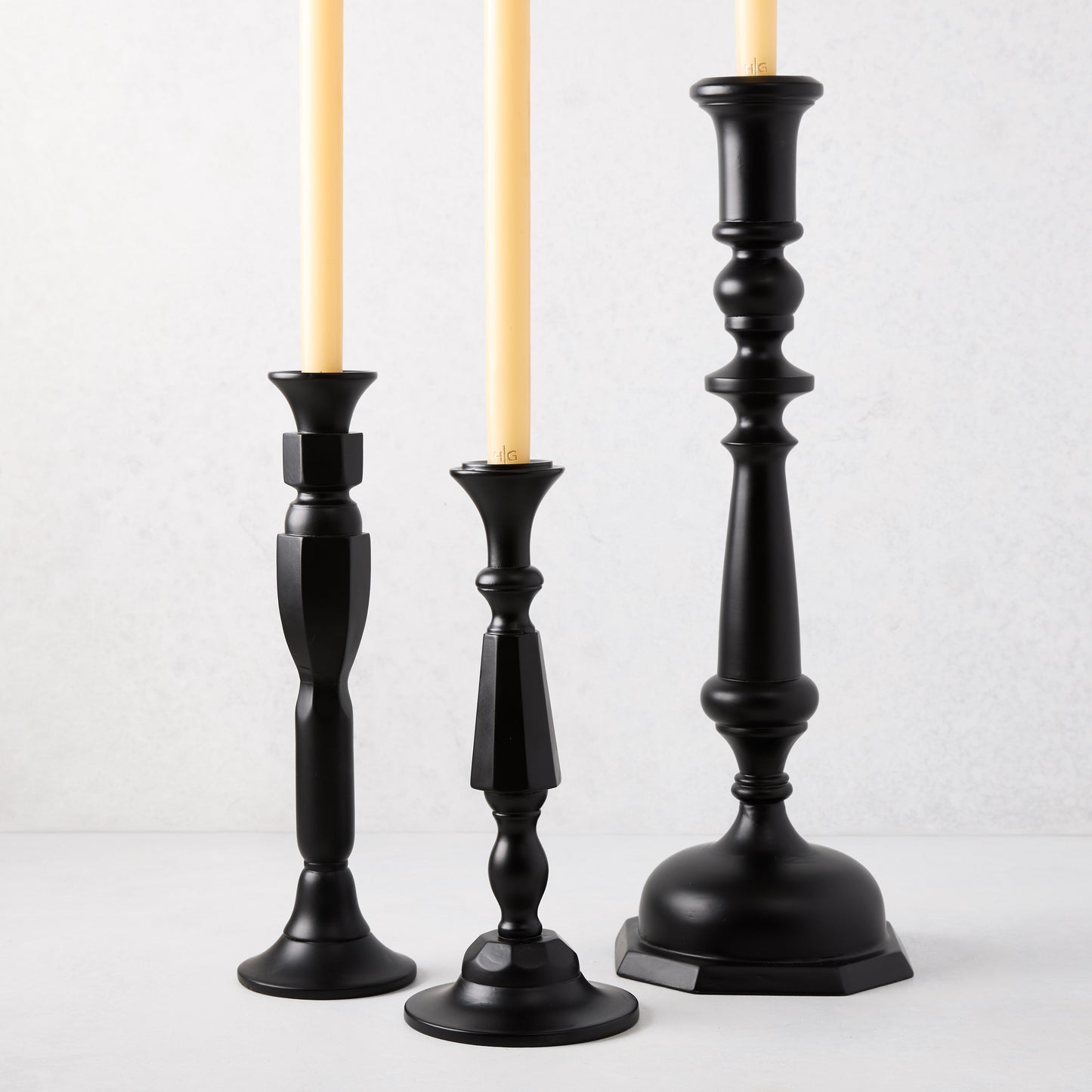 Three black lacquer Georgian candlesticks of varying heights with cream taper candles.
