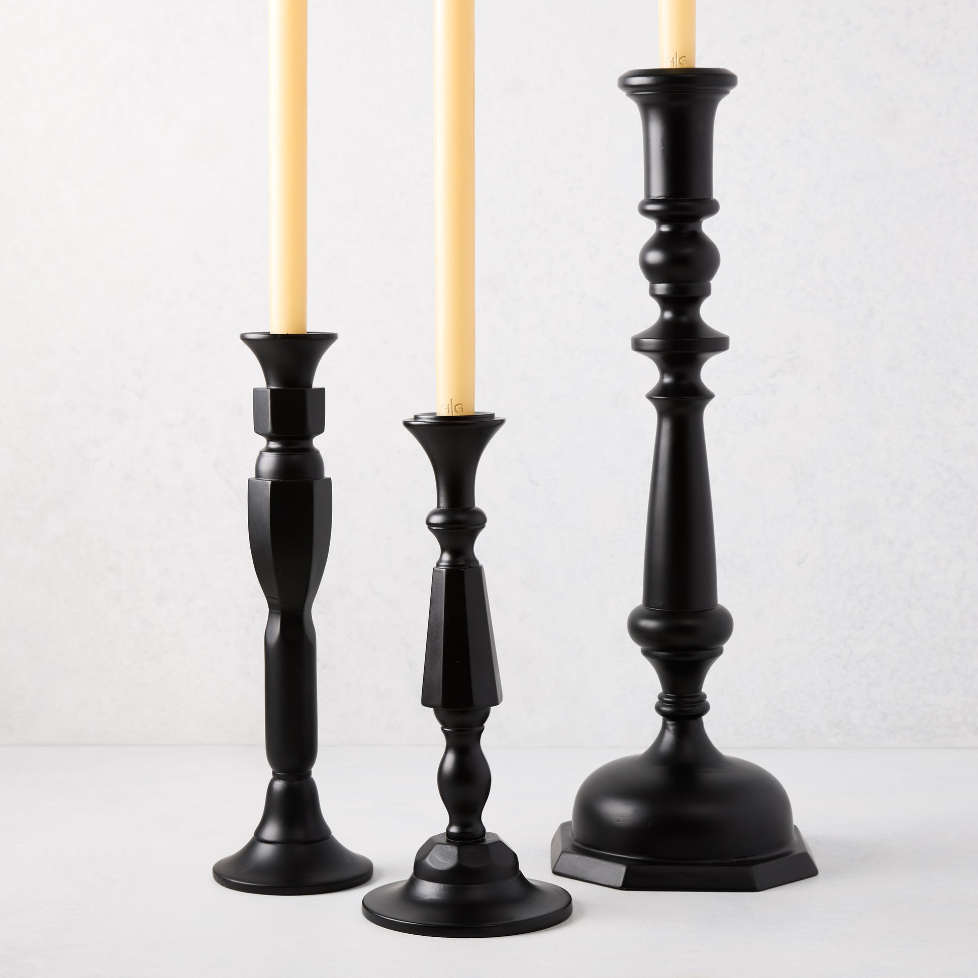 Three black lacquer Georgian candlesticks of varying heights with cream taper candles.