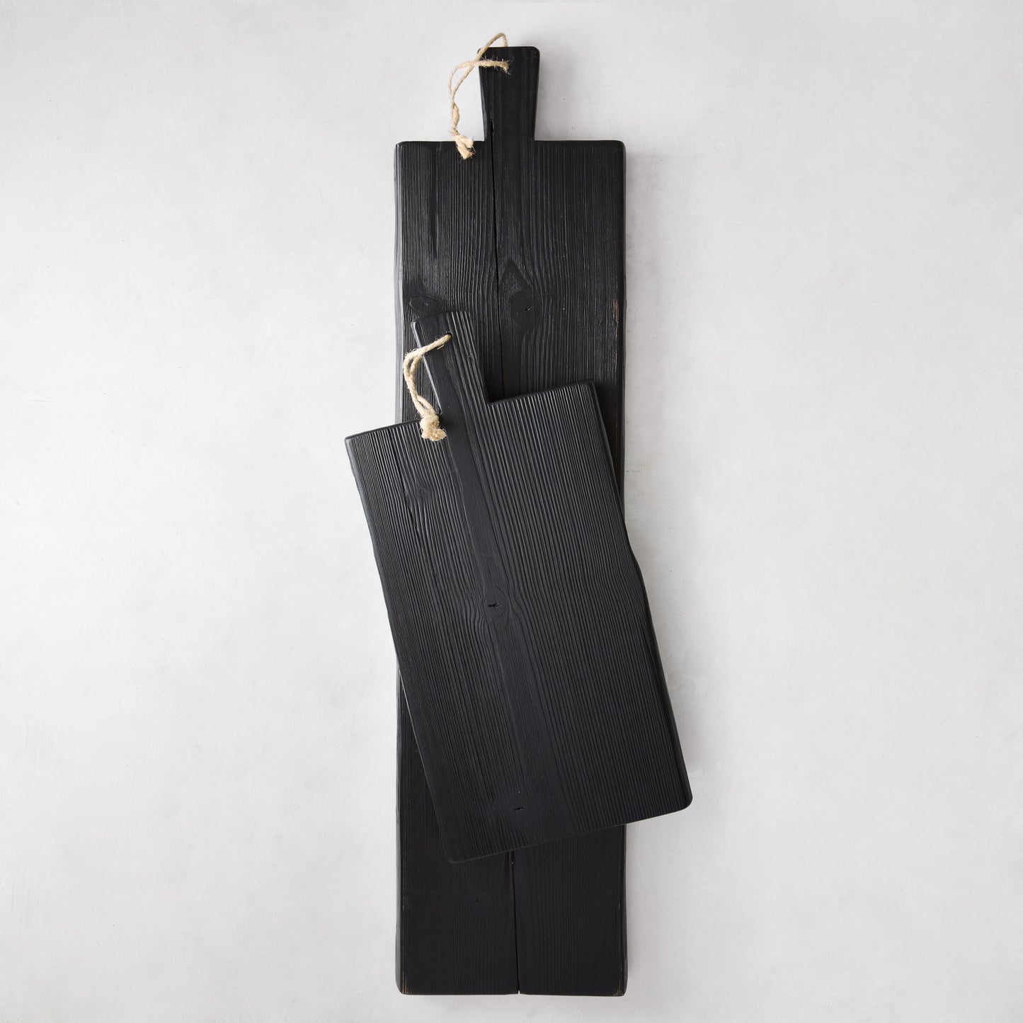 Two black reclaimed wood serving planks, one long and one shorter, with rope hangers.
