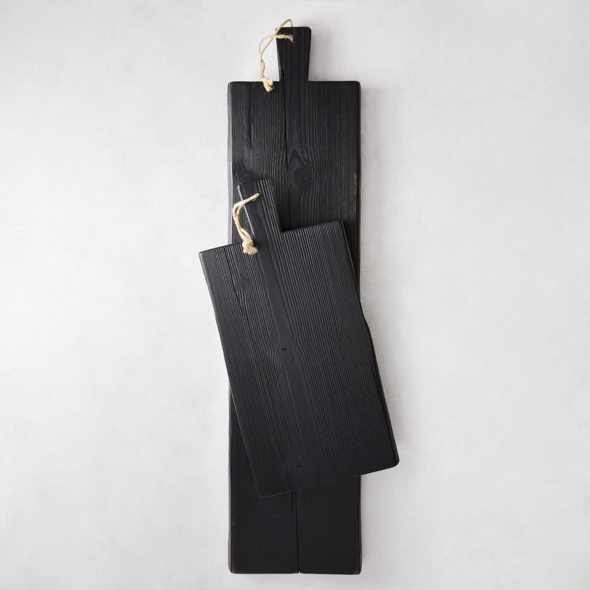 Two black reclaimed wood serving planks, one long and one shorter, with rope hangers.