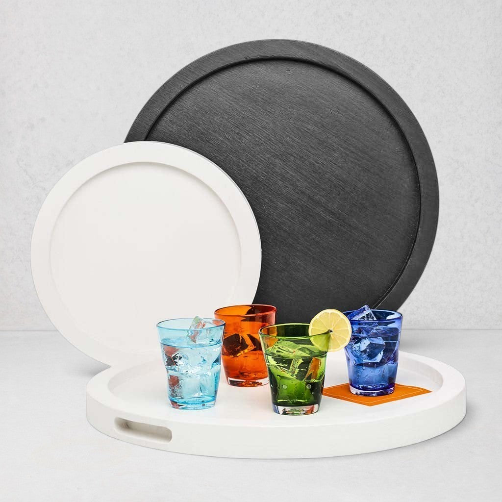 Small round white wood serving tray with cutout handles, holding four colorful drinks. Large gray tray behind.