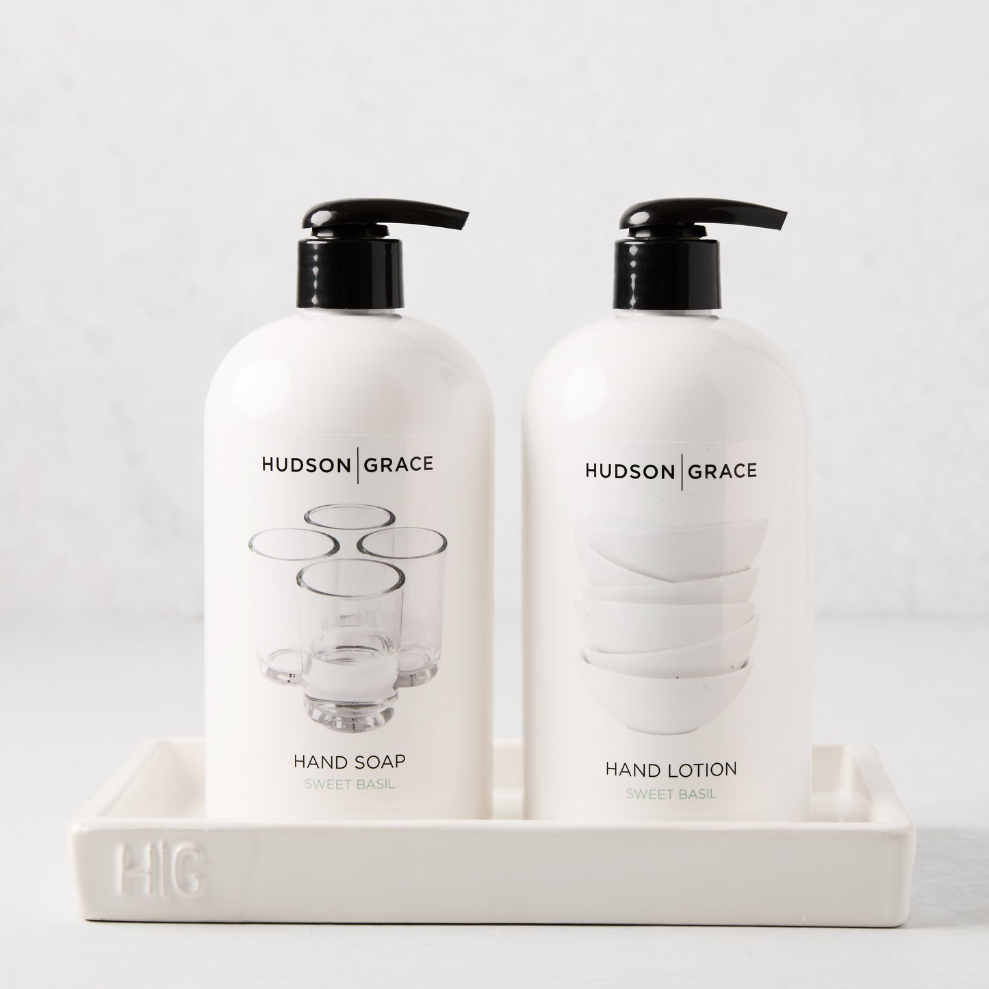 White ceramic tray with "HG" monogram, holding two white Hudson Grace soap and lotion bottles.