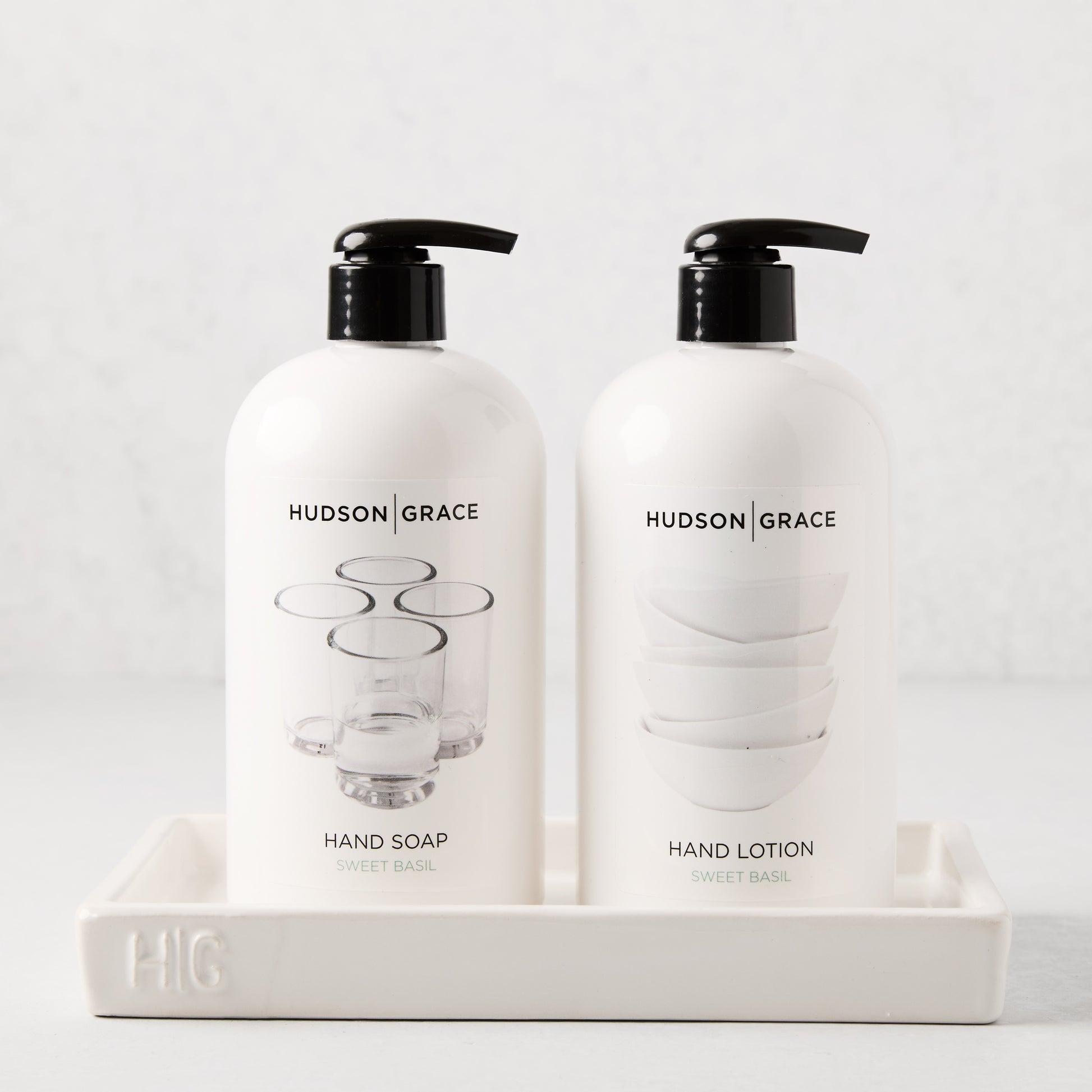 White ceramic tray with "HG" monogram, holding two white Hudson Grace soap and lotion bottles.