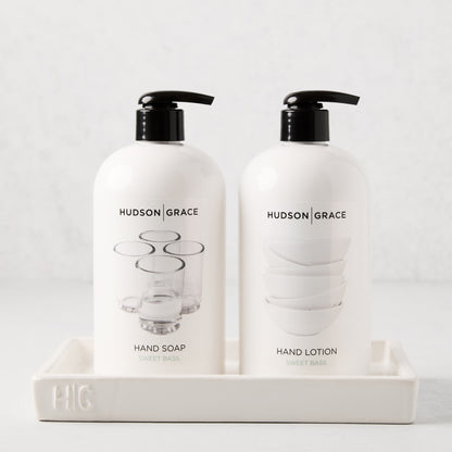 White ceramic tray with "HG" monogram, holding two white Hudson Grace soap and lotion bottles.