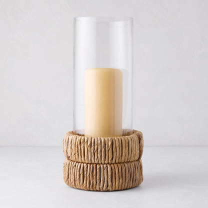 Small glass hurricane with a handwoven banana bark base and an amber candle.