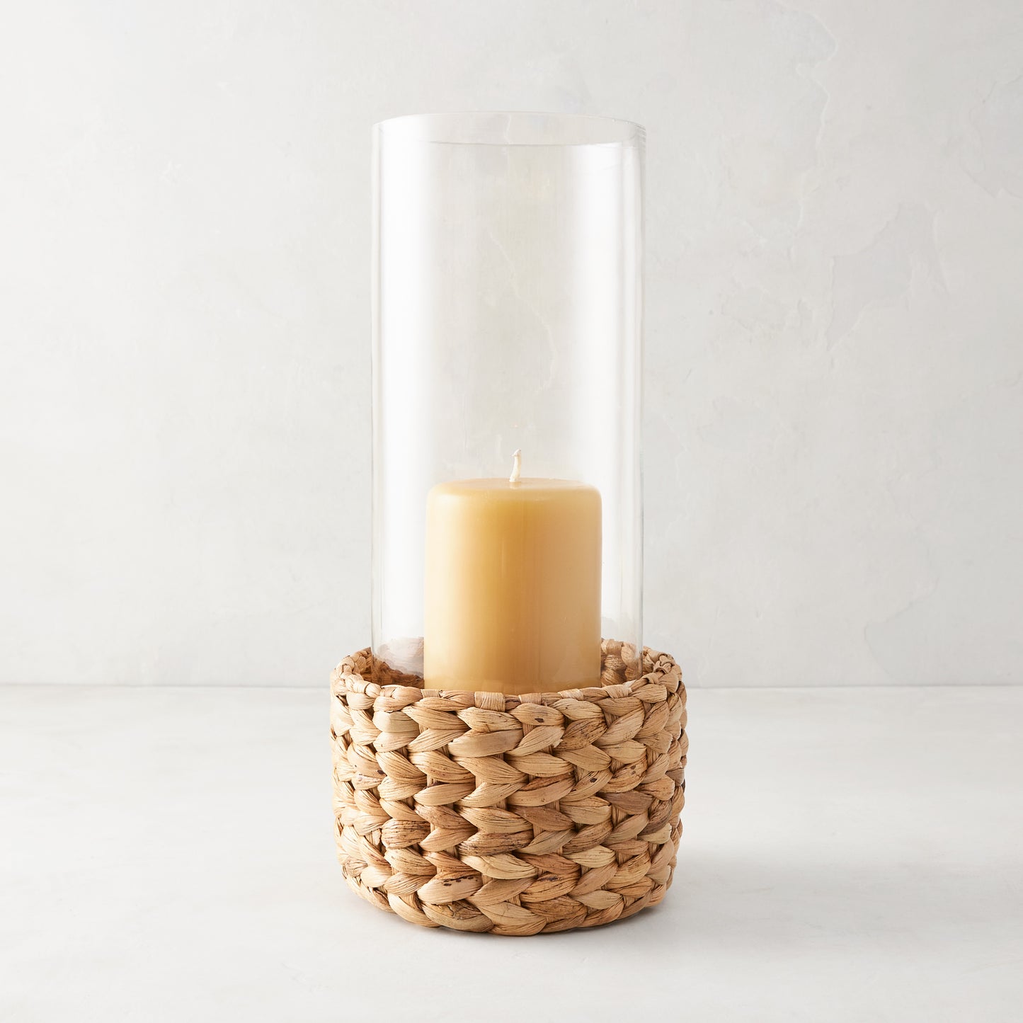 Small glass hurricane with a handwoven natural water hyacinth base and an amber candle inside.