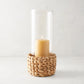 Small glass hurricane with a woven water hyacinth base and a lit amber candle.