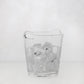 Small clear handblown glass ice bucket with integrated handles, filled with ice cubes.