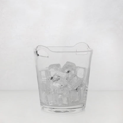 Small clear handblown glass ice bucket with integrated handles, filled with ice cubes.
