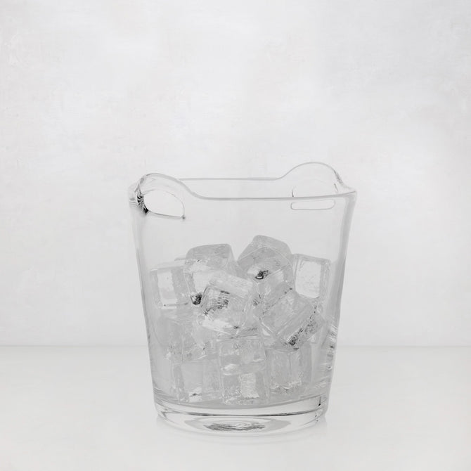 Small clear handblown glass ice bucket with integrated handles, filled with ice cubes.
