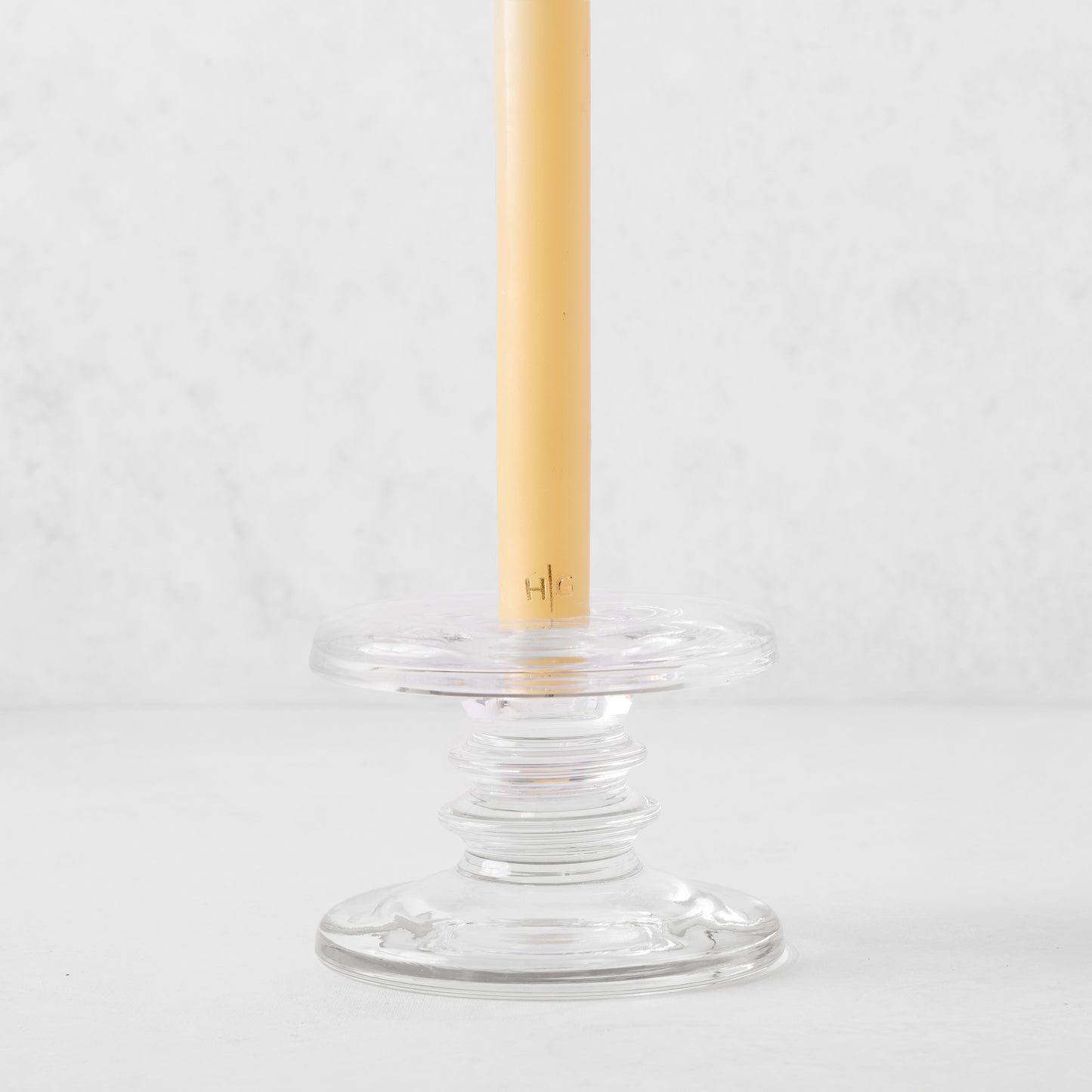 Small clear glass single candleholder with ridges, holding a beige taper candle.