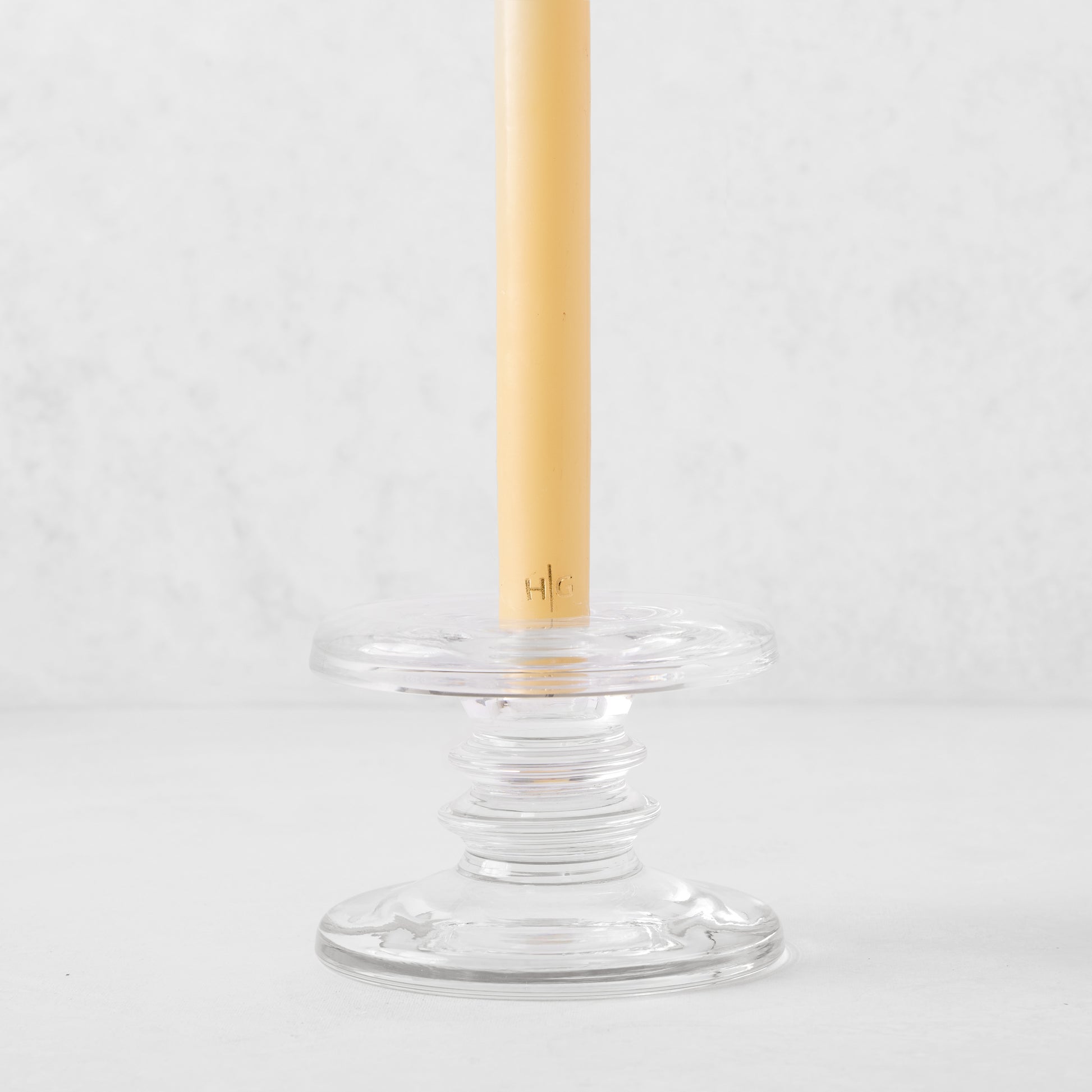Small clear glass single candleholder with ridges, holding a beige taper candle.