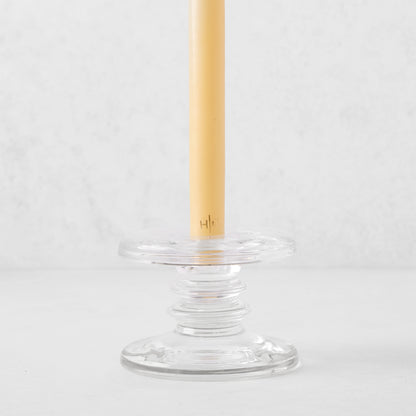 Small clear glass single candleholder with ridges, holding a beige taper candle.