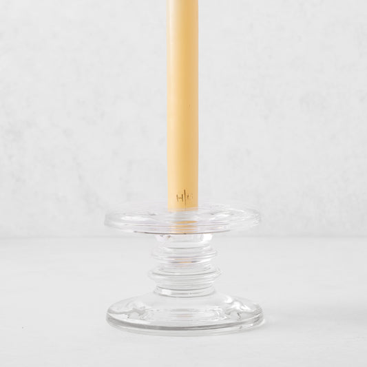 Small clear glass single candleholder with ridges, holding a beige taper candle.