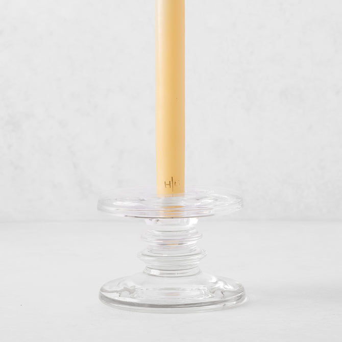 Small clear glass single candleholder with ridges, holding a beige taper candle.
