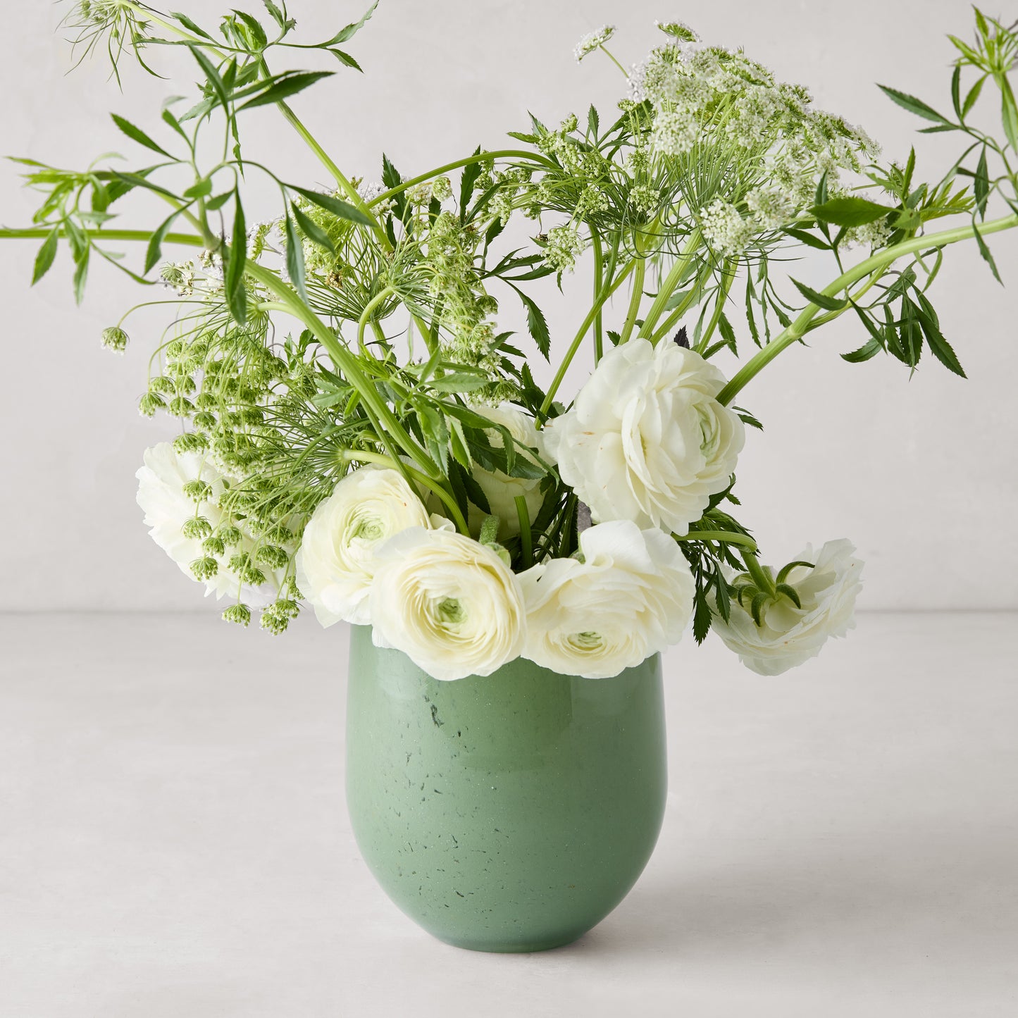 Small opaque green barrel glass vase with white ranunculus and greenery.