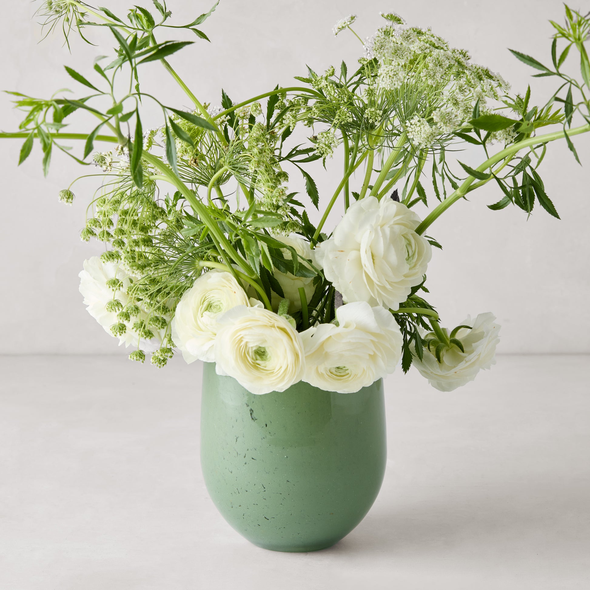 Small opaque green barrel glass vase with white ranunculus and greenery.