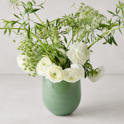 Small opaque green barrel glass vase with white ranunculus and greenery.