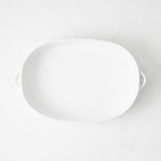 Small white oval stoneware baker with side handles, viewed from above on a light background.